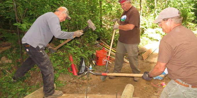 Three Sammamish stewards hard at work with shovels in a wooded area on a trail.