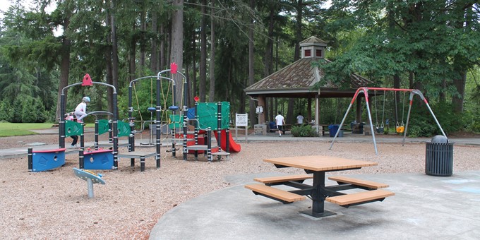 ebright creek park playground, with swingset and play structure over wood chip surface, in front of covered picnic shelter